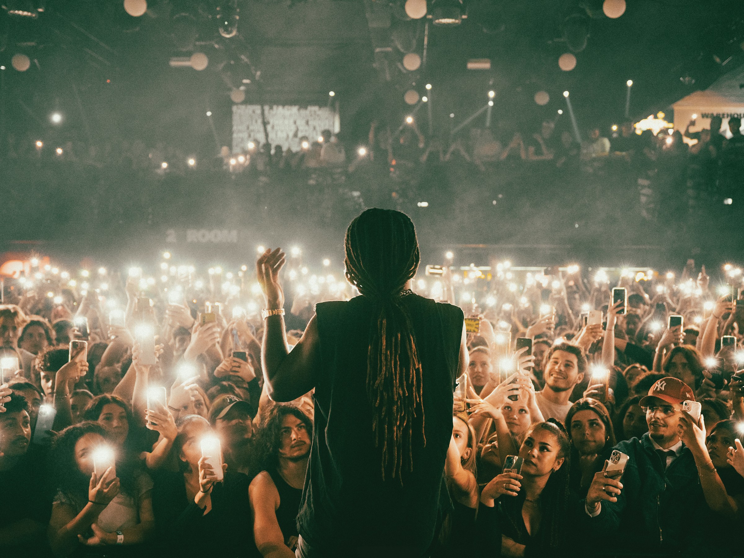 A performer on stage facing a crowd holding up glowing phones